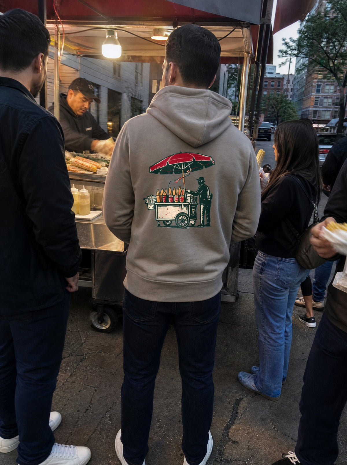 Man in a Mushroom El Elote Hoodie, back view, at a street elote cart with friends