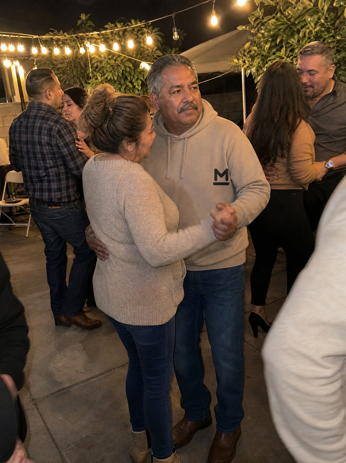 Man in a Mushroom La Música Hoodie dancing with his wife under string lights