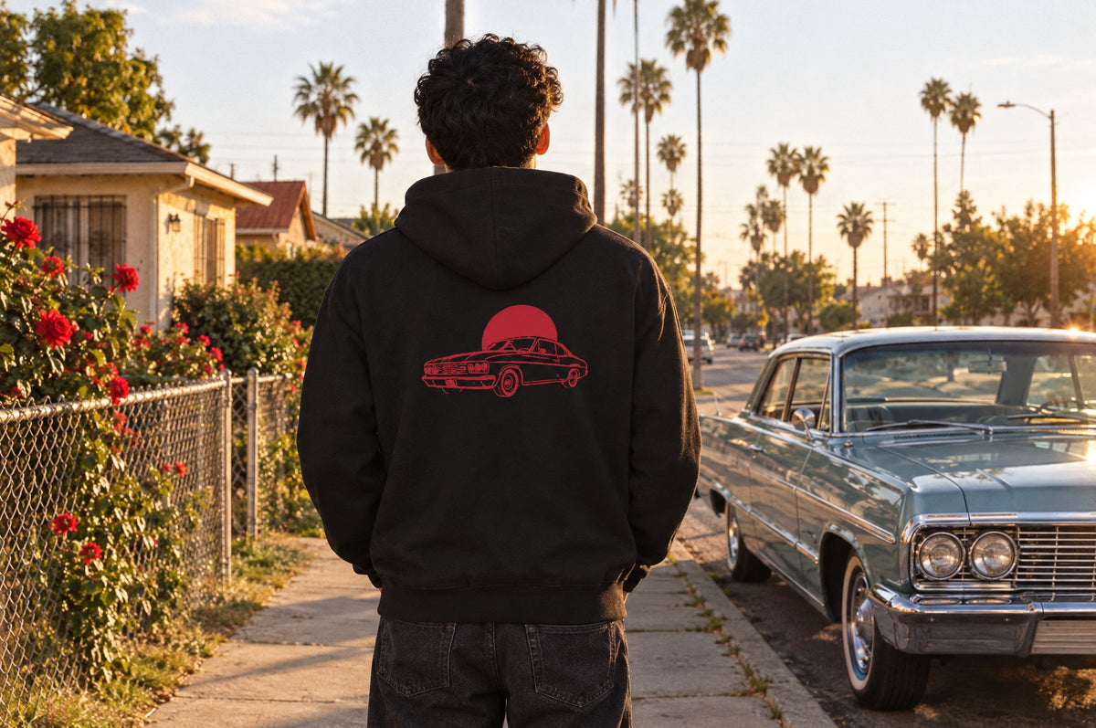 The Del Barrio Hoodie worn on a palm-lined street with a classic car, seen from behind.
