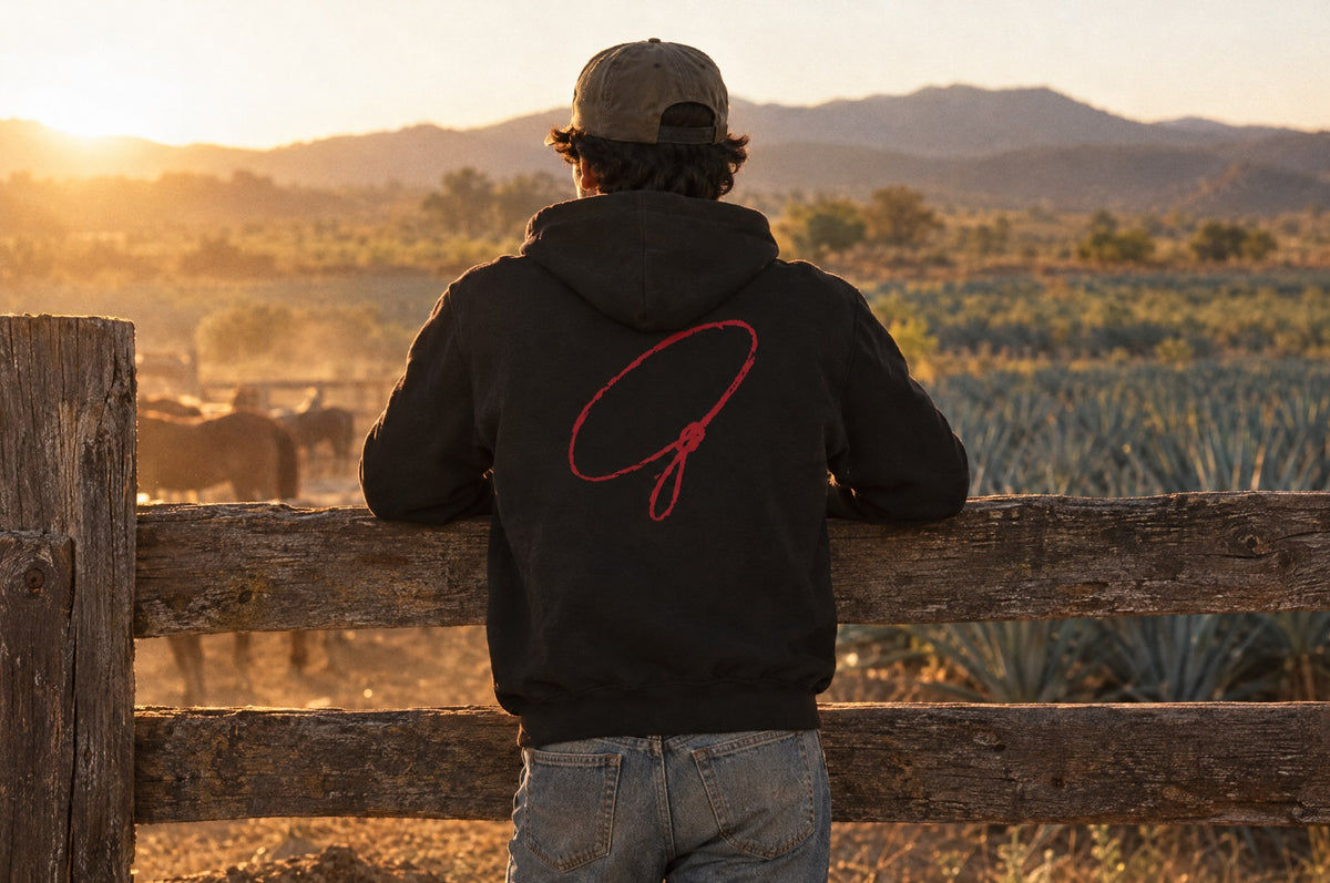 The Del Rancho Hoodie worn at a ranch corral at sunset, seen from behind.
