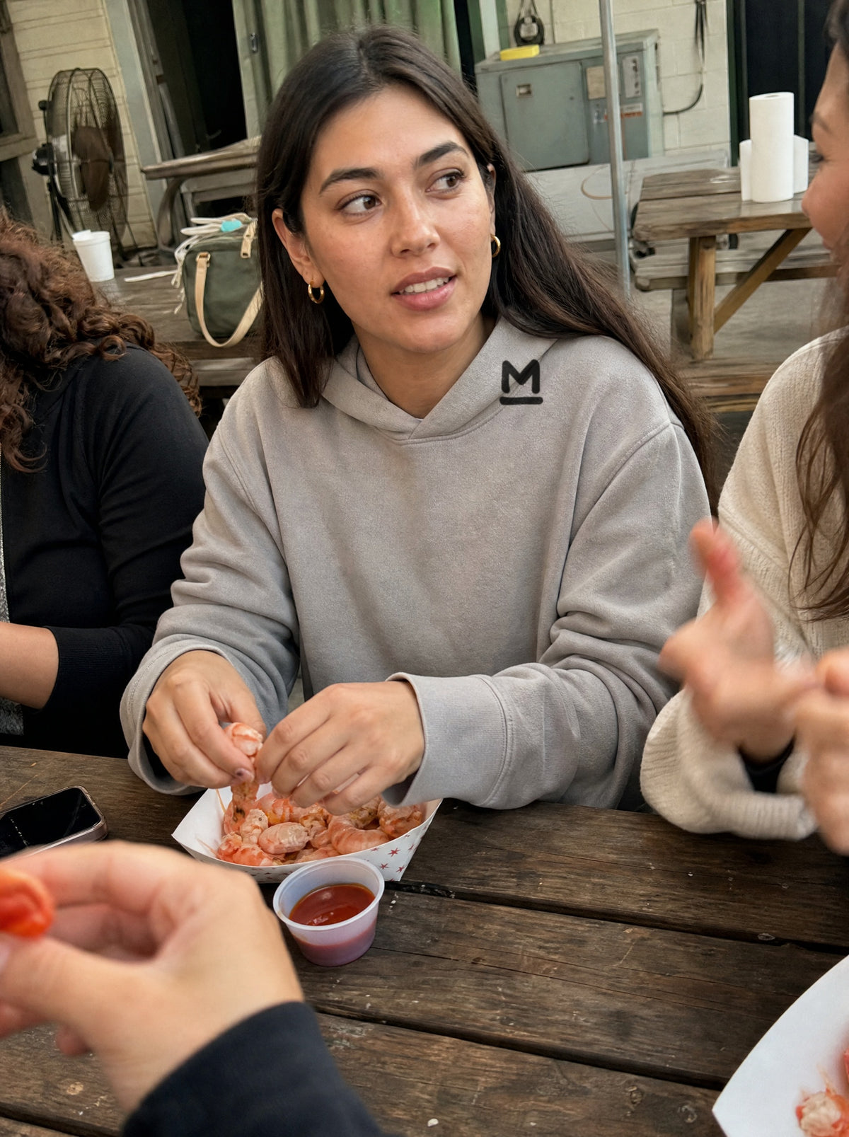 Woman in a Mushroom El Camarón Hoodie peeling shrimp at a picnic table with friends