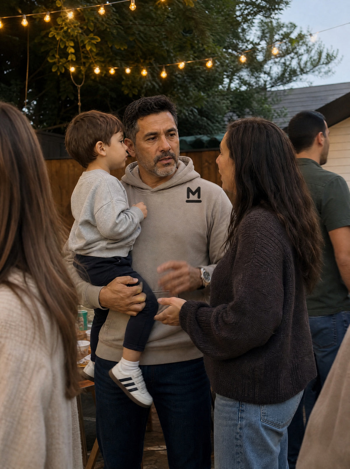 Man in a Mushroom El Mezquite Hoodie holding his nephew at a backyard family party