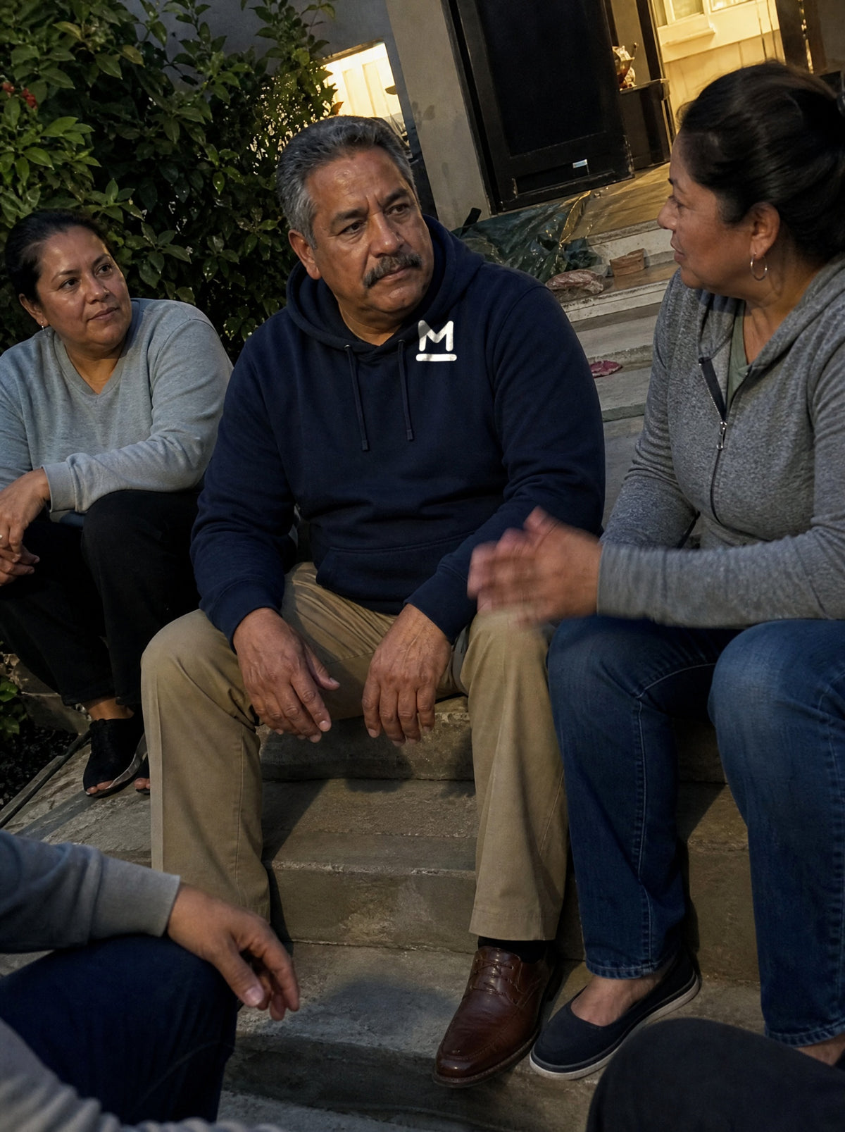 Man in a Navy Blue La Esquina Hoodie talking with neighbors on front steps in the evening